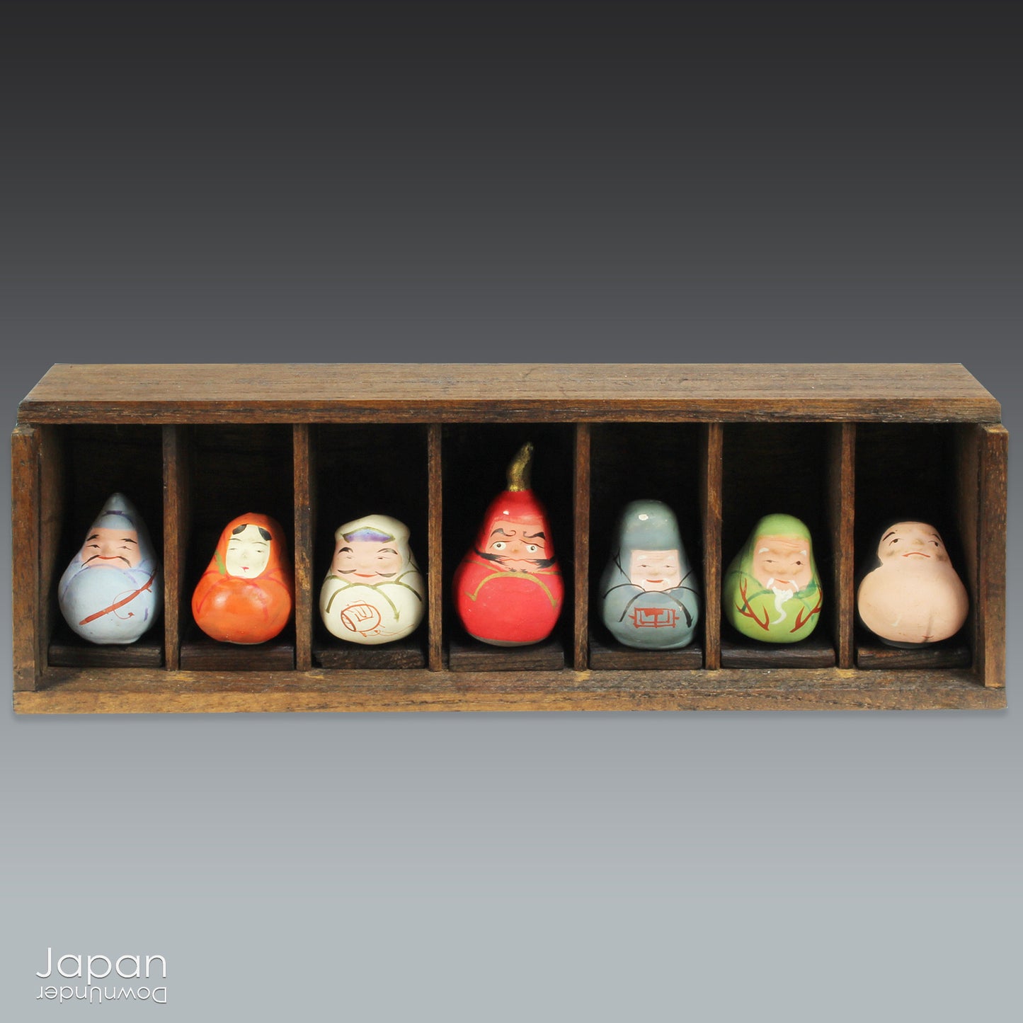 Invite good fortune and timeless tradition into your home with this quaint set of miniature antique Daruma charms. Housed in a charming wooden and glass display box, this unique collection adds an elegant and meaningful touch to your decor, perfect for any space seeking a blend of tradition, luck, and positive energy.

Crafted in the 1920s, this set features hand-painted clay Daruma figures representing the Seven Lucky Gods of Japan, each with its own powerful symbolism.